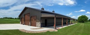 50x80 black gable steel garage shop with three overhead doors, stone accents, cupolas, and a wraparound covered porch in Basehor, KS.